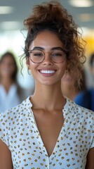 A woman with glasses and a smile on her face. She is wearing a white shirt with a floral pattern