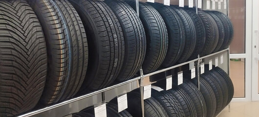 New automotive tires are neatly stacked on metal shelving in a tire shop or auto parts store, displaying various tread patterns and price tags