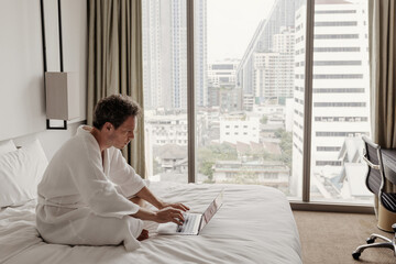 Businessman working on laptop in hotel room, business travel, Man in bathrobe using computer in modern hotel room