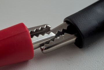 Photo of two alligator clips with red and black handles on white background.