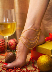 A woman's foot next to a glass of wine and a gift in a box and Christmas tree balls