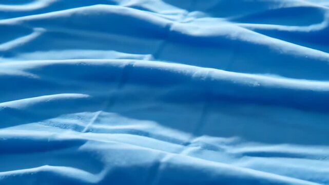 Close-up view of smooth blue fabric with intricate folds and creases creating a dynamic texture