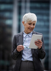 Senior business woman holds tablet and smiles in city area