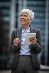 Senior business woman holds tablet and smiles in city area