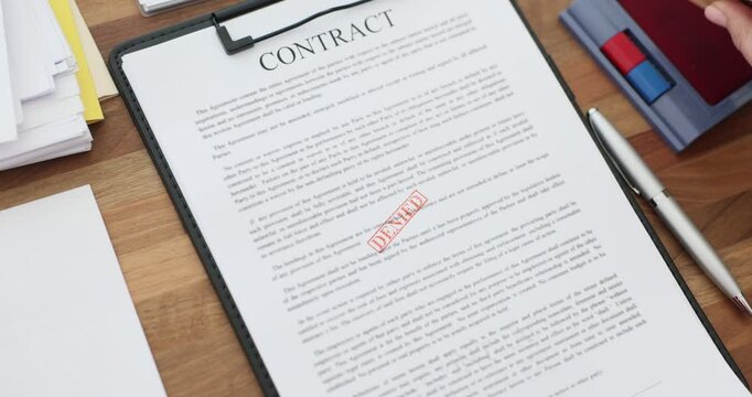 Female hand presses red Denied stamp on contract page with text. Office worker holds clipboard steady while finalizing rejection decision slow motion