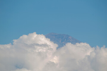 Rocky mountain peak emerging above thick white clouds against a vast blue sky.