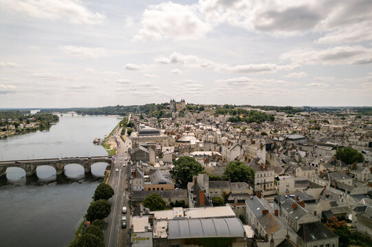 Aerial view of the Loire River snaking past the historic Chateau de Saumur, its stone walls glowing softly under the diffused sunlight, Saumur, Pays de la Loire, France.