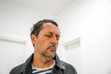 Thoughtful adult male in a clean modern white room, dressed in a leather jacket, captured in a moment of quiet reflection.
