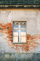 Abandoned house window with peeling plaster and exposed brick