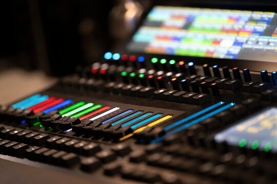 A colorful control panel displays various buttons and graphics in a dark studio. The setup is part of a control room used for managing audio and visual productions during events.