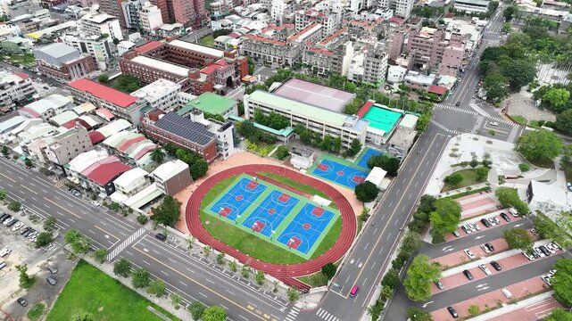 Aerial view of school campus in Taiwan featuring colorful basketball courts, running track, and building with rooftop solar panels. 4K Drone