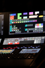 A colorful control panel displays various buttons and graphics in a dark studio. The setup is part of a control room used for managing audio and visual productions during events.