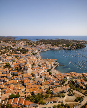 Aerial view of terracotta rooftops cascade to meet the turquoise bay dotted with boats, a vibrant tapestry under the bright Spanish sun, Cadaques, Catalonia, Spain.