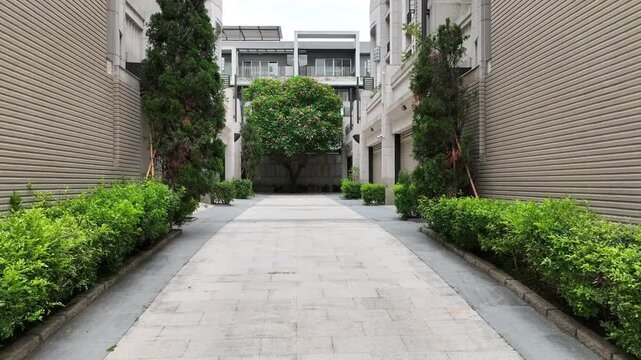 Low aerial dolly shot moving through an opening modern metal gate, revealing a private luxury townhouse courtyard and landscaped path. 4K