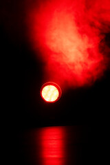 Bright red lights pierce through swirling smoke in a dimly lit space, creating an intense...