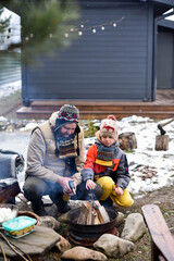 Father and son lighting a fire with a gas gun in the backyard, dressed in winter clothes