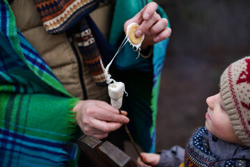 Joyfully surprised boy in winter clothes looking at roasted marshmallow in adult hands