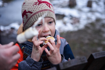 Boy in winter clothes eating roasted marshmallow with cookies