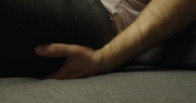 Close-up scene of a person sitting on a sofa and reacting to skin itching or discomfort, illustrating everyday irritation, restlessness, and common health or hygiene issues in daily life.