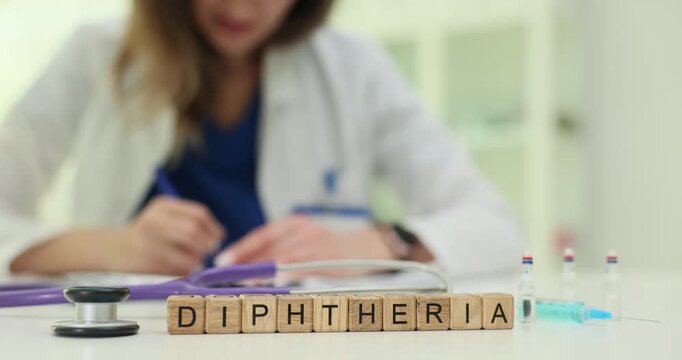 Wooden blocks on table spell Diphtheria beside syringes and vials. Woman doctor fills vaccination form preparing immunization plan for patient