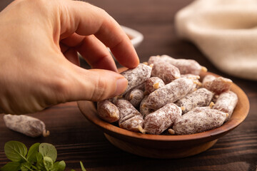Small smoked Chicken sausages in wooden bowl with hand on brown wooden. side view, close up, selective focus