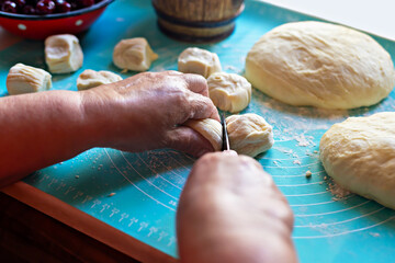 Cooking pies. Hands of elderly baker skillfully cutting dough into small pieces on turquoise countertop, surrounded by flour and fresh cherries, creating warm and inviting baking atmosphere