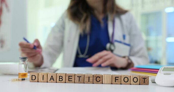 Wooden blocks on white desk spell words Diabetic Foot near vial. Woman doctor checks chart while writing notes about ulcer treatment for patient