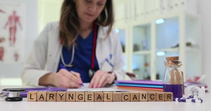 Wooden blocks spell words Laryngeal Cancer on medical table. Woman doctor writes report reviewing throat tumor treatment plan at appointment
