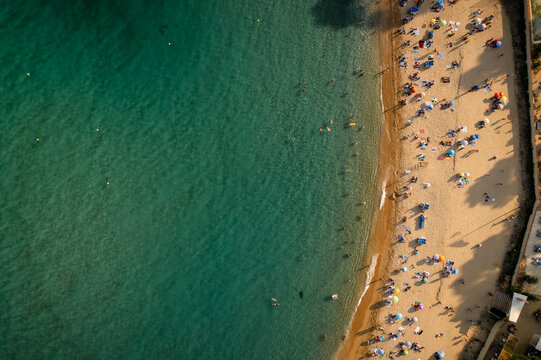 Aerial view of the golden sands meeting the turquoise waters, dotted with sunbathers and colorful umbrellas, Lloret de Mar, Catalonia, Spain.
