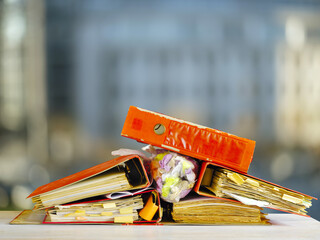 Messy file folders, ring binders grungy paperwork.Red tape, bureaucracy, overworked, beat the clock business concept on blurred office building background.Free copy space.