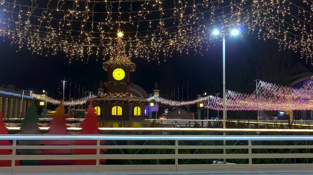 Festive Christmas Market Square Illuminated by Holiday String Lights, Nighttime winter fair featuring decorated pavilion, glowing clock tower, joyful atmosphere