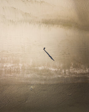 Aerial view of a solitary figure casts a long shadow on the rippled, textured sands of Camber Sands Beach, England, United Kingdom.