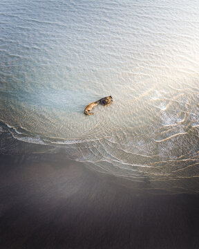 Aerial view of a stranded shipwreck in the gentle surf, the meeting point of dark sands and shimmering waters, Camber Sands, England, United Kingdom.