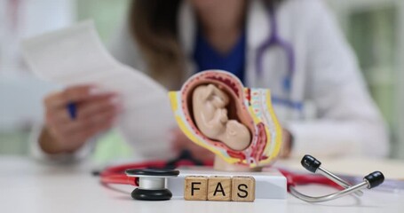 Letters FAS on cubes with stethoscope and fetus anatomic model in hospital. Woman gynecologist with ultrasound scans analyses fetal alcohol syndrome