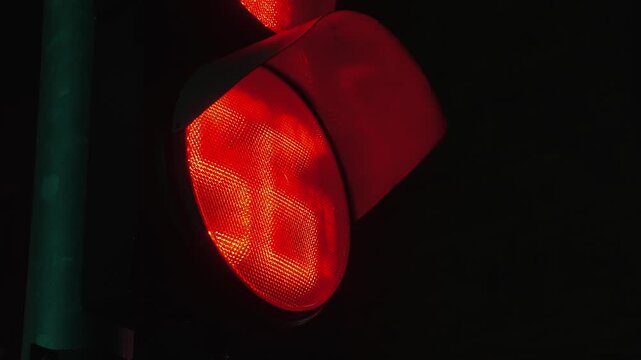 Close-up of a pedestrian traffic light countdown timer at night. Green signal changes to blinking and then red with numeric countdown. Urban street safety concept, time limit and decision making.