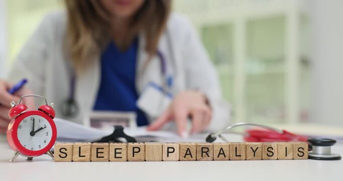 Phrase Sleep Paralysis on wooden blocks and vi9ntage alarm clock against working doctor. Physician reads patient medical records in hospital