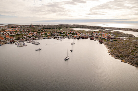Aerial view of boats gently bobbing in the harbor under a sky of pearl and ash, the red-roofed buildings of the town nestled against the rocky coastline, Smogen, Vastra Gotaland County, Sweden.
