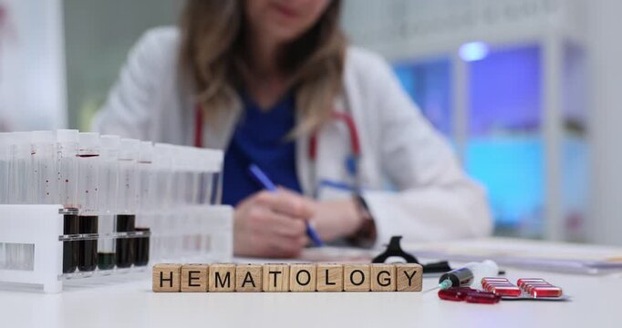 Word Hematology on wooden cubes with blood samples in tubes and medications in hospital. Woman doctor checks ultrasound scans in medical lab