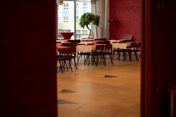Empty Red Cafe Dining Room With Rows Of Wooden Tables And Chairs, Parquet Floor, Vase Of Flowers On Central Table Near Window, Soft Sunlight Creating