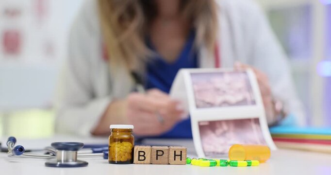 Letters BPH on wooden cubes near stethoscope and pills in hospital. Woman physician controls benign prostatic hyperplasia development in clinic