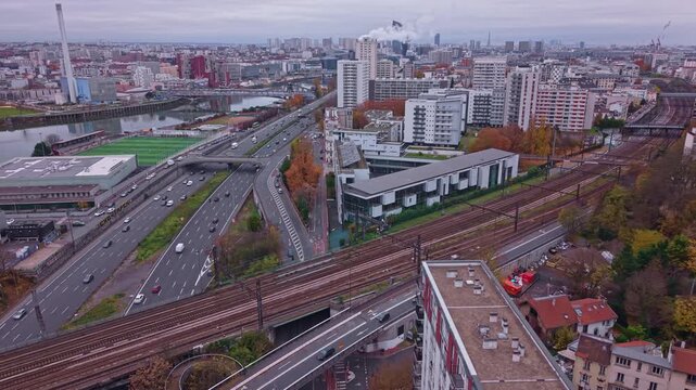 Aerial drone view of highway traffic and railway tracks in Saint-Maurice near Paris. Features the Marne River, Ivry incinerator, and urban skyline in autumn. Ideal for infrastructure concepts, France
