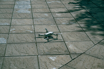 Drone placed on paved sidewalk tiles, ready for takeoff in an urban outdoor setting.