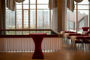 Empty Foyer With Tall Windows And Standing Table Covered In Red Linen, City Skyline Visible Through Glass Panes Minimal Reception Setup Under Soft