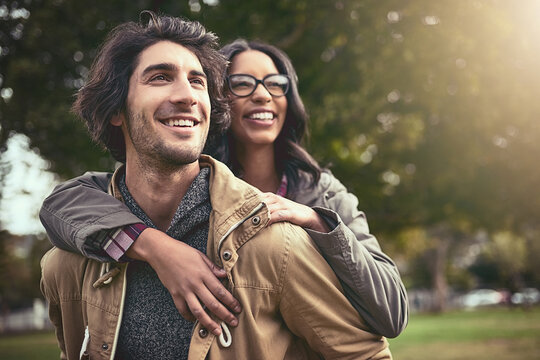 Couple, piggy back and smile in park with care, bonding or thinking on adventure in spring on holiday. Interracial love, man and woman with hug, playful and outdoor on vacation with game in Toronto