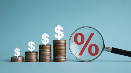 Stacks of coins with dollar signs rising, viewed through magnifying glass with percentage sign implies investment interest grow