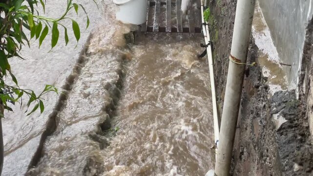 High angle view of muddy flood water overflowing from a small drainage ditch during heavy rain.
