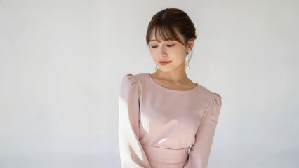 Obraz premium 淡色ピンクの長袖ワンピースを着た美しい女性が、まとめ髪で斜め下に視線を向ける