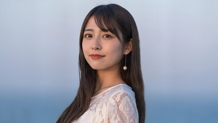 淡い色合いのレース調トップスを着た美しい女性が、黒髪ロングで夕方の光を受けながら静かに視線を向ける