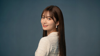 白いニット風トップスを着た美しい女性が、振り返ってカメラにやさしく微笑んでいる