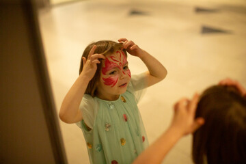 child applying butterfly makeup in mirror, colorful face design and focused expression, soft indoor lighting, pastel dress